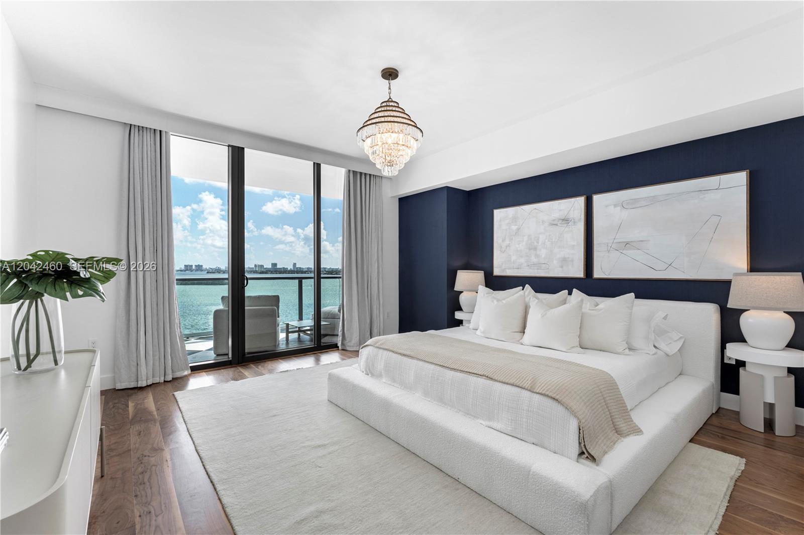 A bedroom features a white platform bed, navy accent wall, and floor-to-ceiling windows overlooking water — 788 NE 23rd St # 902, Miami FL 33137, MIAMI, FL