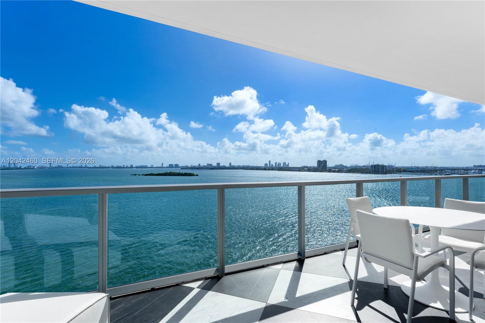 A balcony with a glass railing overlooks the ocean and a distant city skyline — 788 NE 23rd St # 902, Miami FL 33137, MIAMI, FL