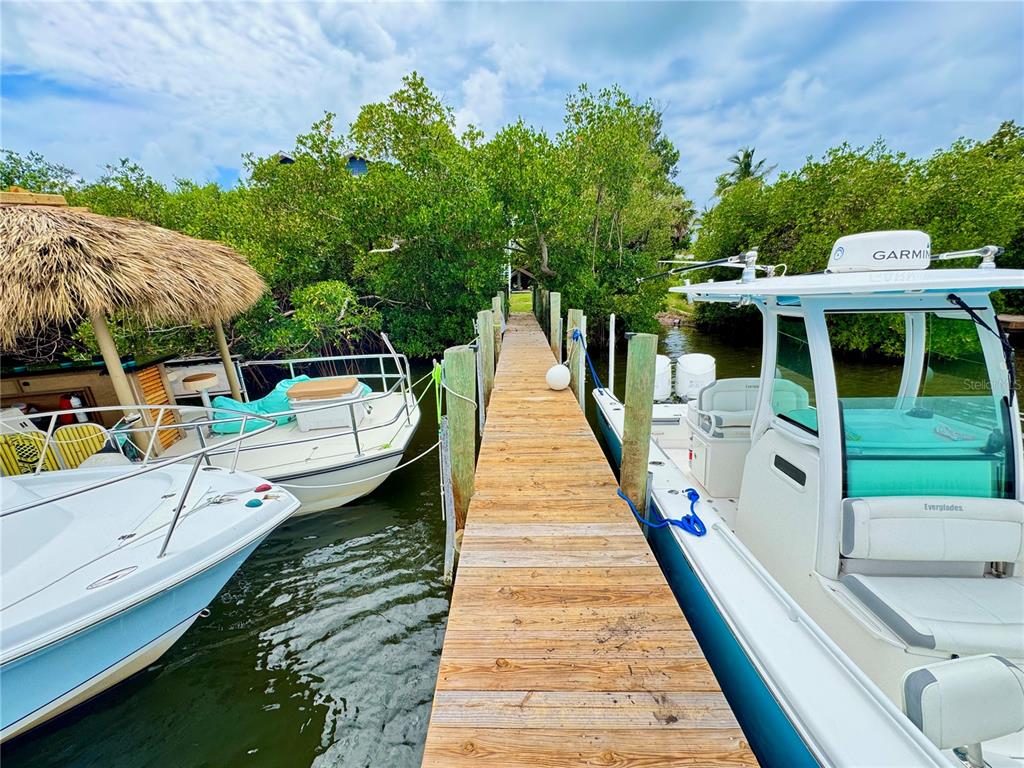 A wooden dock sits between two boats moored in a canal lined with mangrove trees — 8164, 8168, 8158, 8156 LITTLE GASPARILLA ISLAND, PLACIDA, FL