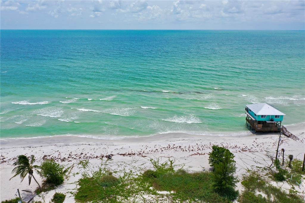 An aerial view shows a stilt house on a sandy beach beside the turquoise ocean — 8164, 8168, 8158, 8156 LITTLE GASPARILLA ISLAND, PLACIDA, FL