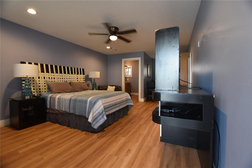 A bedroom features blue walls, wood-look flooring, a ceiling fan, and a black media console — 704 S LAKESHORE BOULEVARD, HOWEY IN THE HILLS, FL