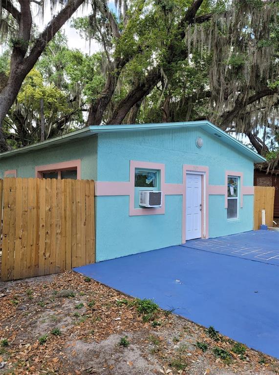 A light blue house with pink trim and a wooden fence sits on a blue driveway — 107 E CYPRESS STREET, KISSIMMEE, FL