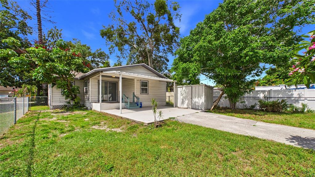 The exterior of a small, light-colored house features a concrete patio and a storage shed — 5457 72ND AVENUE N, PINELLAS PARK, FL