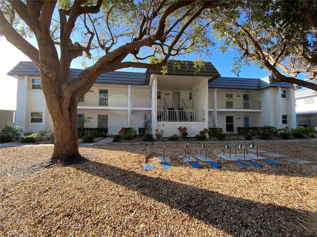 A two-story apartment building exterior features a gravel yard, large trees, and metal railings — 10431 WATERBIRD WAY UNIT 10431, BRADENTON, FL
