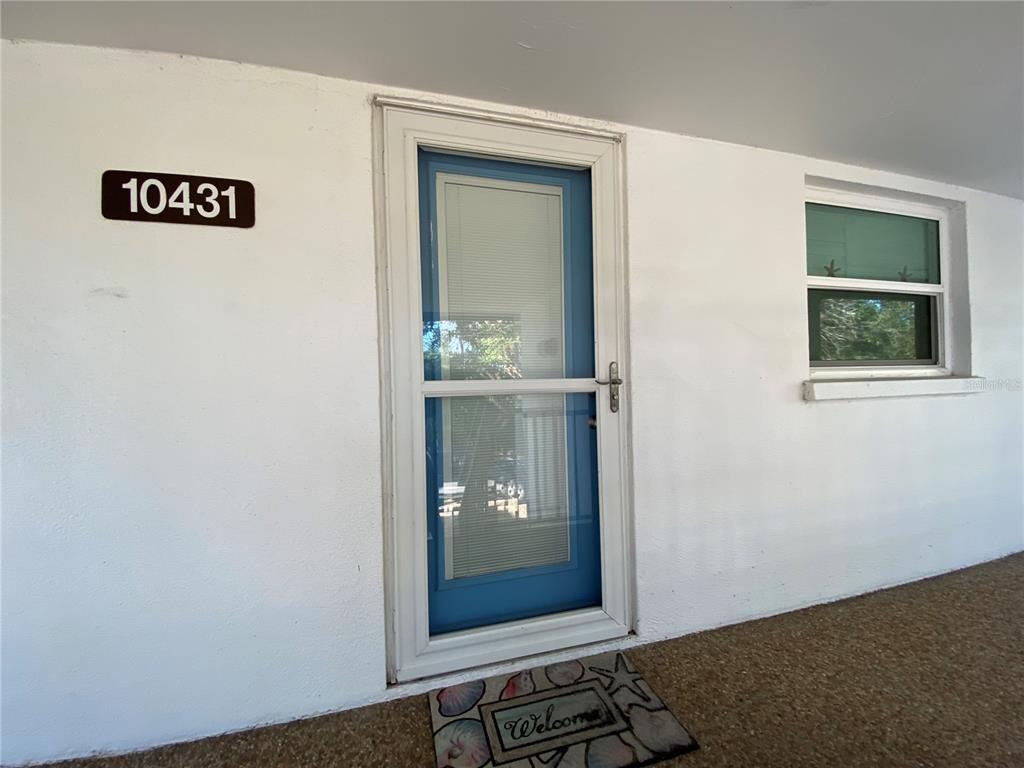 A white exterior wall features a blue storm door, a window, and a welcome mat — 10431 WATERBIRD WAY UNIT 10431, BRADENTON, FL