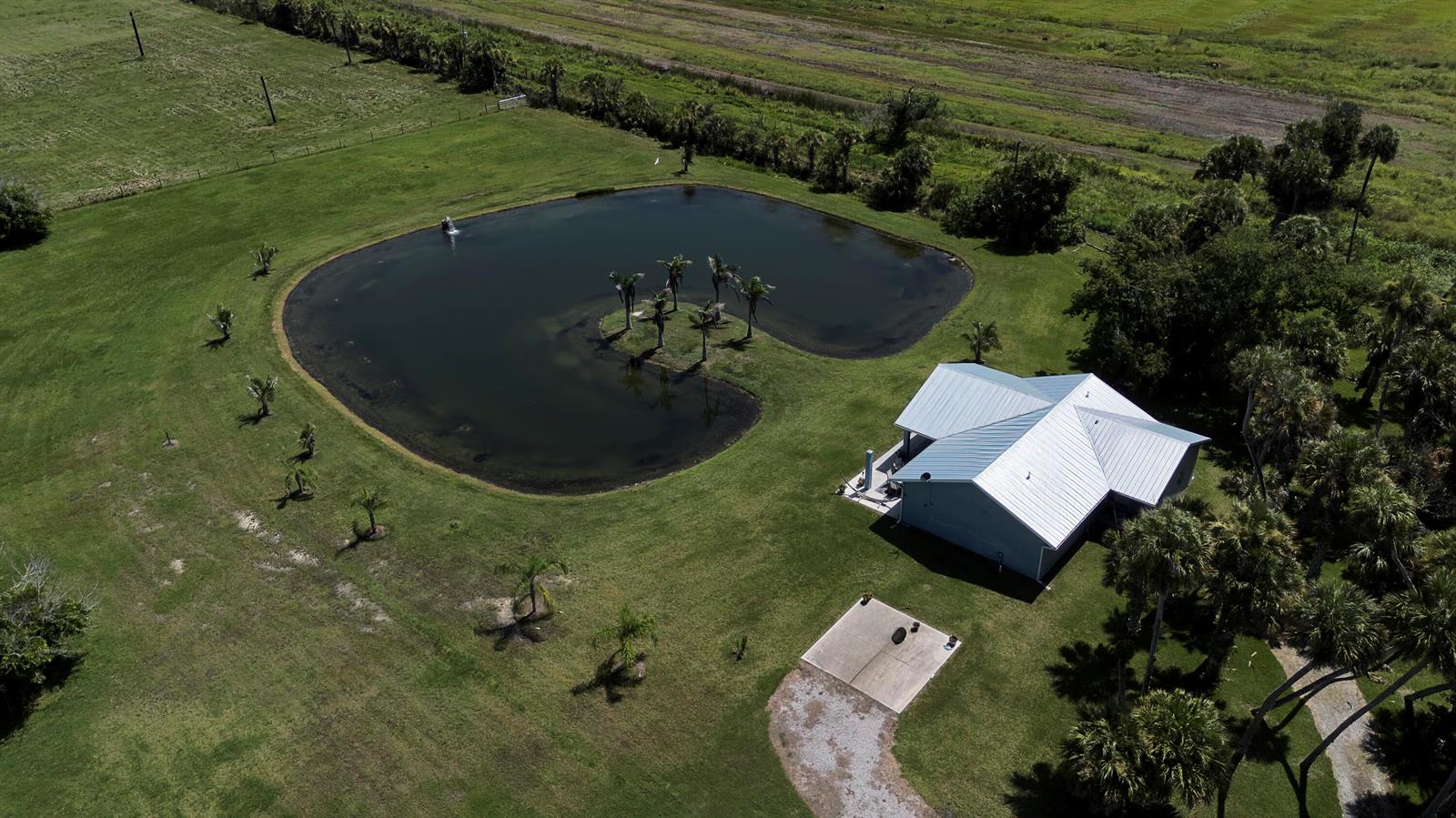 An aerial view shows a house with a metal roof next to a pond — 18601 Orange Avenue, Fort Pierce FL 34945, FORT PIERCE, FL