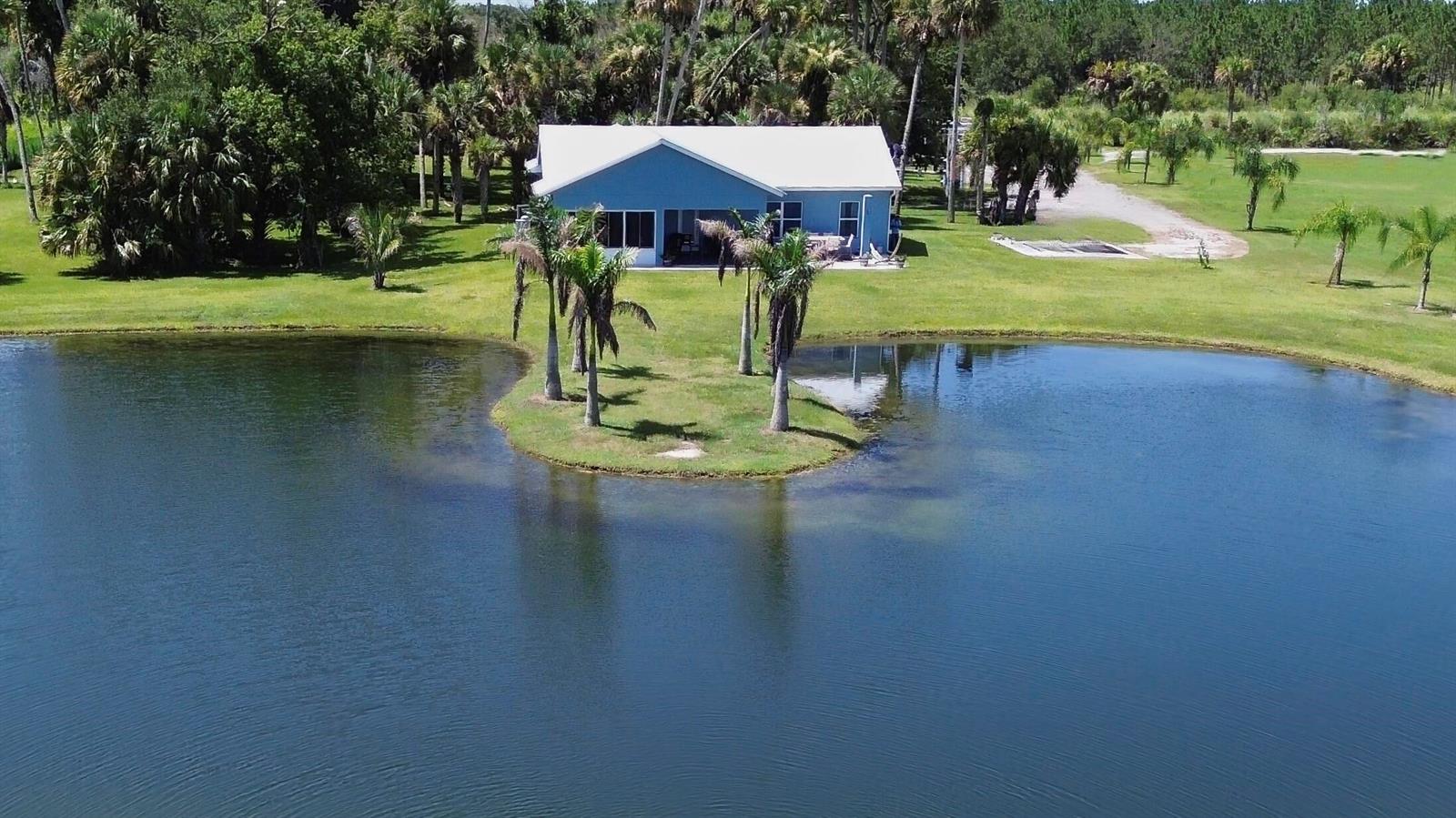 An aerial view shows a blue house with a white roof beside a pond — 18601 Orange Avenue, Fort Pierce FL 34945, FORT PIERCE, FL