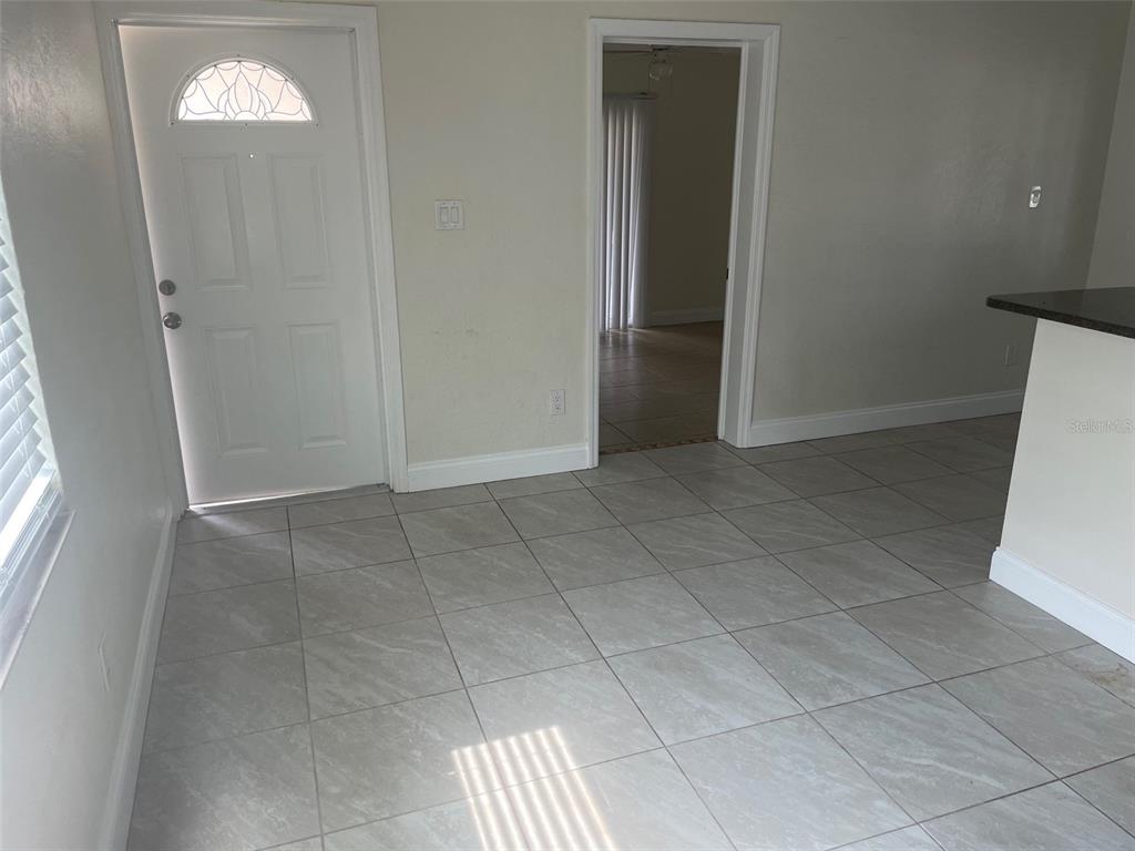 A room with light-colored tile flooring, a white front door, and a doorway leading inside — 5066 3RD STREET N, ST PETERSBURG, FL