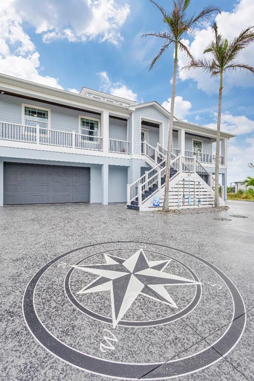 A light blue elevated house with a garage and a compass rose painted on the driveway — 16176 LA BARGE CIRCLE, PORT CHARLOTTE, FL