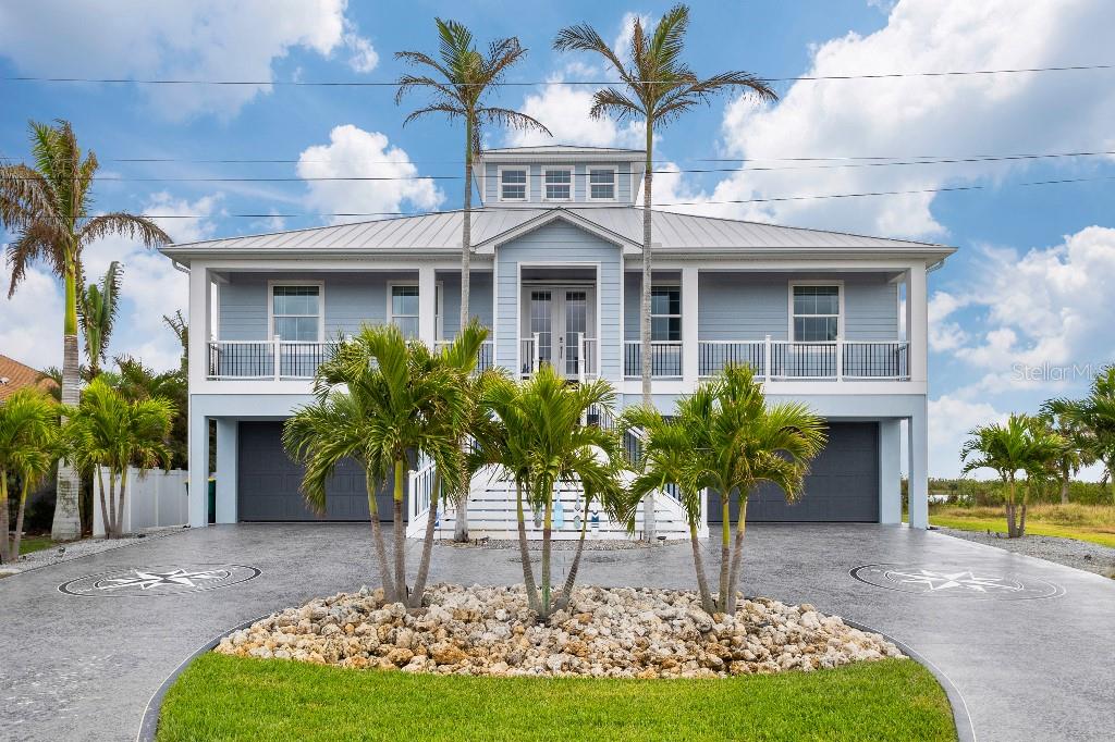 A two-story coastal home with a metal roof, elevated living area, and palm-lined driveway — 16176 LA BARGE CIRCLE, PORT CHARLOTTE, FL