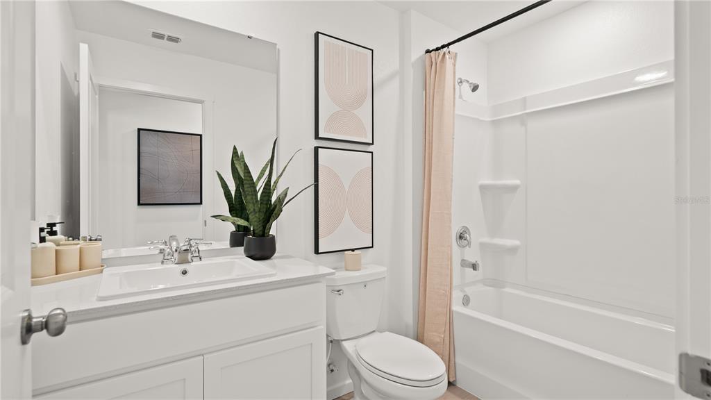 A bright bathroom features a white vanity, a toilet, and a shower-tub combination — 6109 SWAMP BAY DRIVE, EDGEWATER, FL