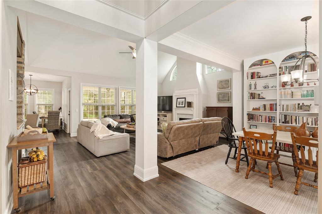 An open-concept living and dining area with wood-look flooring, built-in bookshelves, and a fireplace — 5512 NW 51ST AVENUE, GAINESVILLE, FL