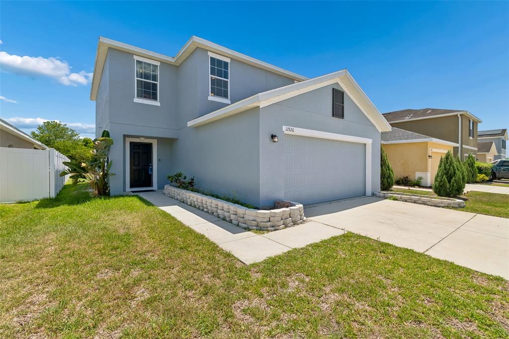 A two-story house with light gray stucco siding, a two-car garage, and a concrete driveway — 11926 GRAND KEMPSTON DRIVE, GIBSONTON, FL