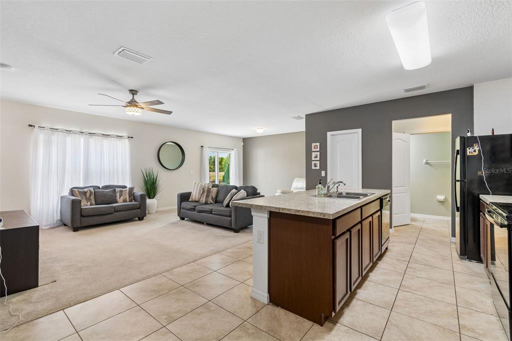 An open-concept living room with carpeted floors flows into a kitchen featuring a central island — 11926 GRAND KEMPSTON DRIVE, GIBSONTON, FL