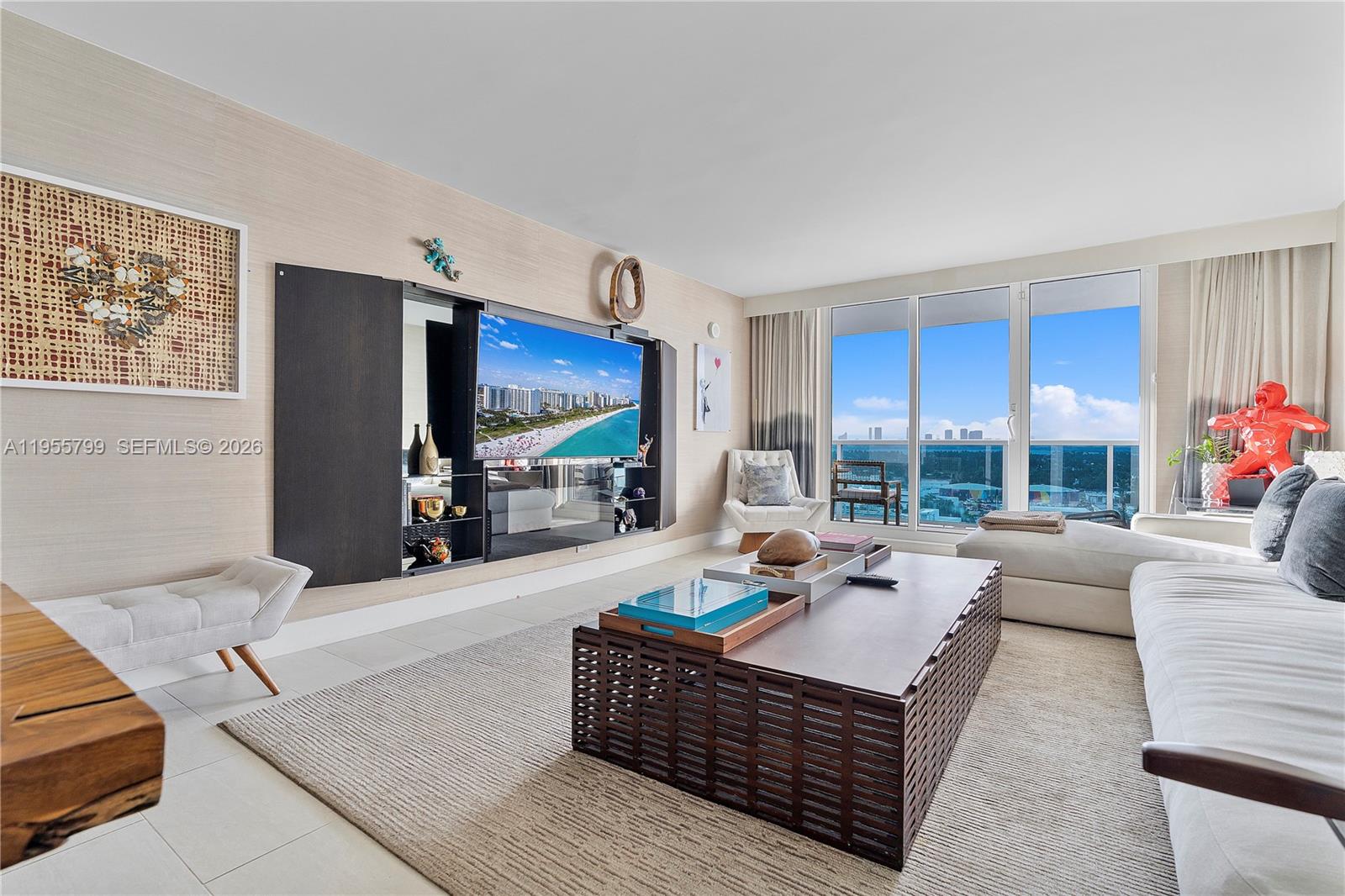 A modern living room features a large television, a slatted coffee table, and floor-to-ceiling windows — 102 24th St # 1427, Miami Beach FL 33139, MIAMI BEACH, FL