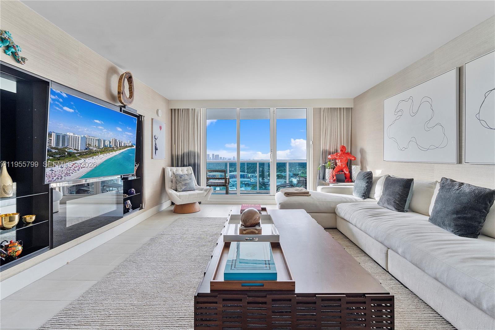 A modern living room features a large sectional sofa, a television, and a balcony view — 102 24th St # 1427, Miami Beach FL 33139, MIAMI BEACH, FL