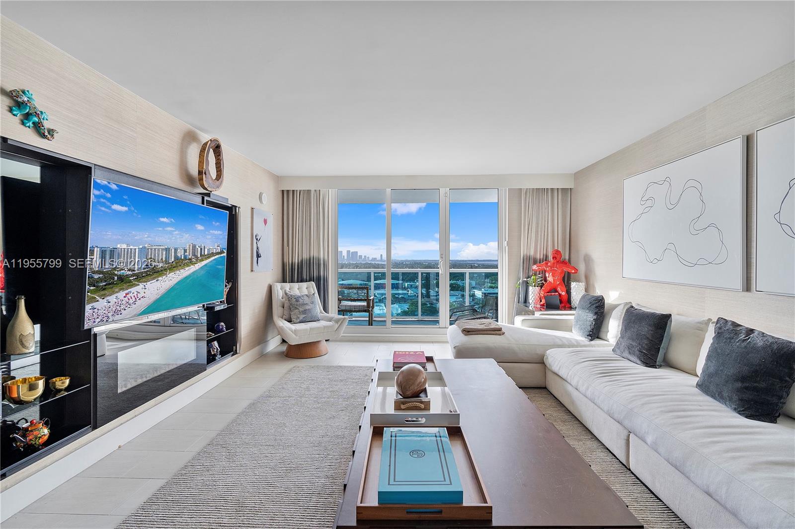 A modern living room features a large sectional sofa, a wall-mounted television, and balcony views — 102 24th St # 1427, Miami Beach FL 33139, MIAMI BEACH, FL