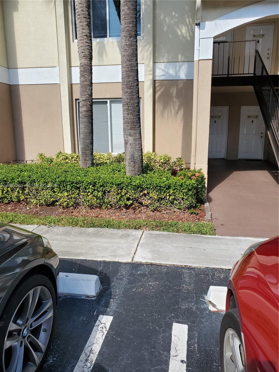 The exterior of a multi-story apartment building features palm trees, landscaping, and parking spaces — 815 W Boynton Beach Blvd # 102, Boynton Beach FL 33426, BOYNTON BEACH, FL