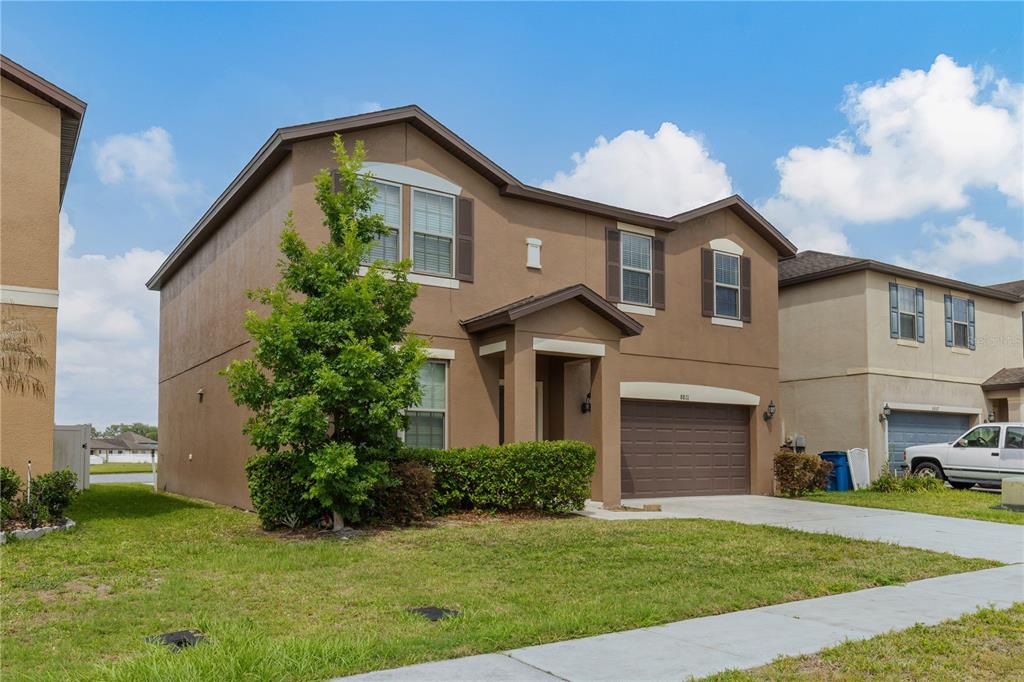 A two-story tan stucco house with a brown garage and a front lawn — 8811 ASHLAND AVENUE, POLK CITY, FL