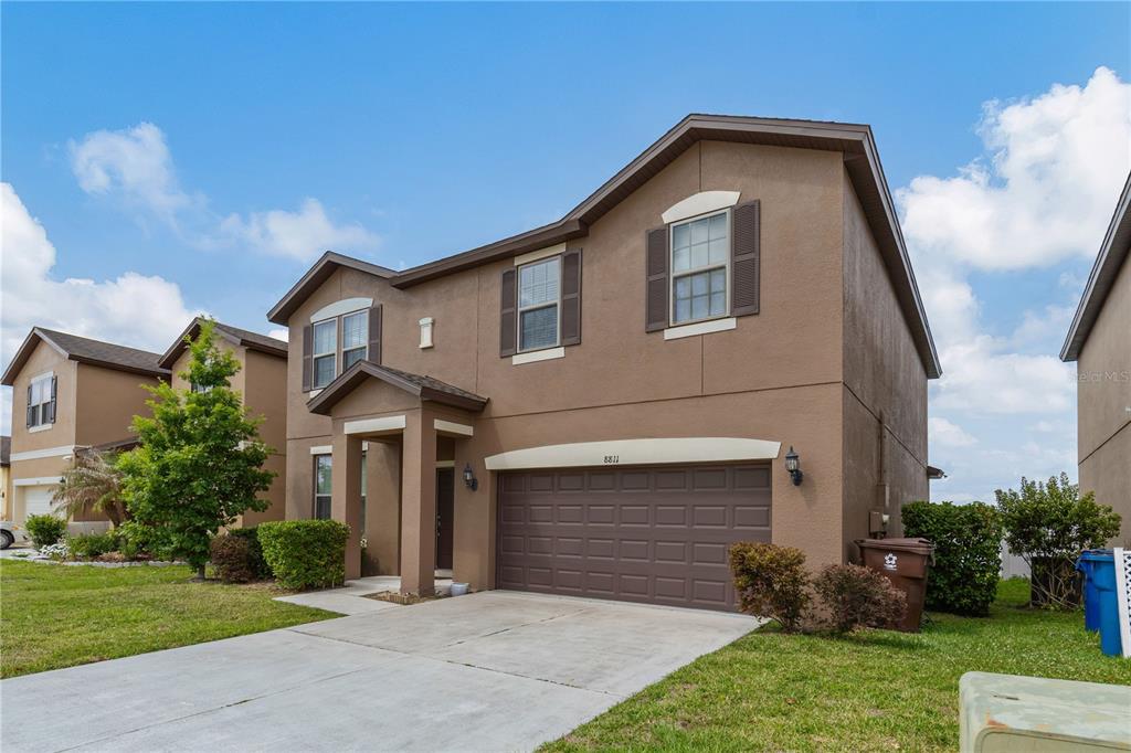 A two-story brown stucco house features a two-car garage and a covered front entryway — 8811 ASHLAND AVENUE, POLK CITY, FL