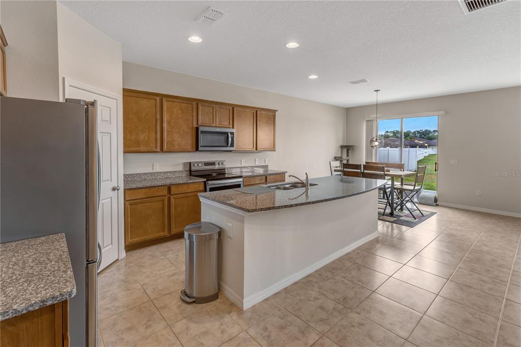 A kitchen with wood cabinets, granite countertops, a center island, and a dining area — 8811 ASHLAND AVENUE, POLK CITY, FL