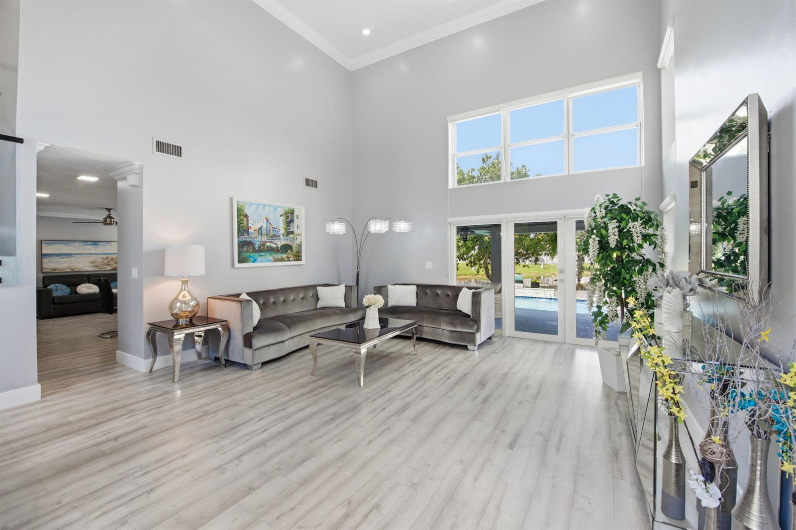 A high-ceiling living room features grey velvet sofas, light wood flooring, and large windows — 14040 Richwood Place, Davie FL 33325, DAVIE, FL