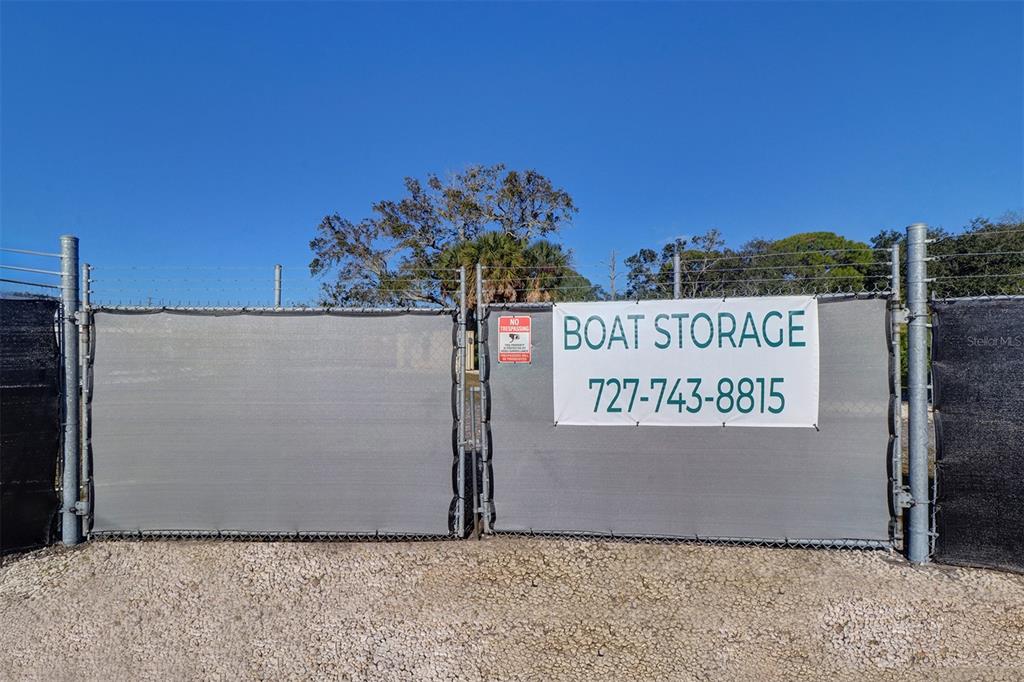 A chain-link fence with privacy screening and a boat storage sign stands on a gravel lot — 332 ANCLOTE ROAD, TARPON SPRINGS, FL