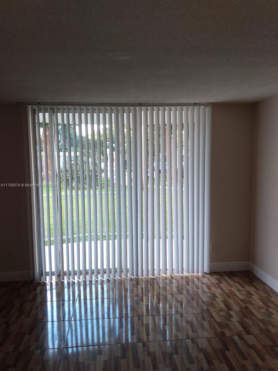 A room with tiled floors and vertical blinds covering a large sliding glass door — 494 NW 165th St Rd # 102, Miami FL 33169, MIAMI, FL