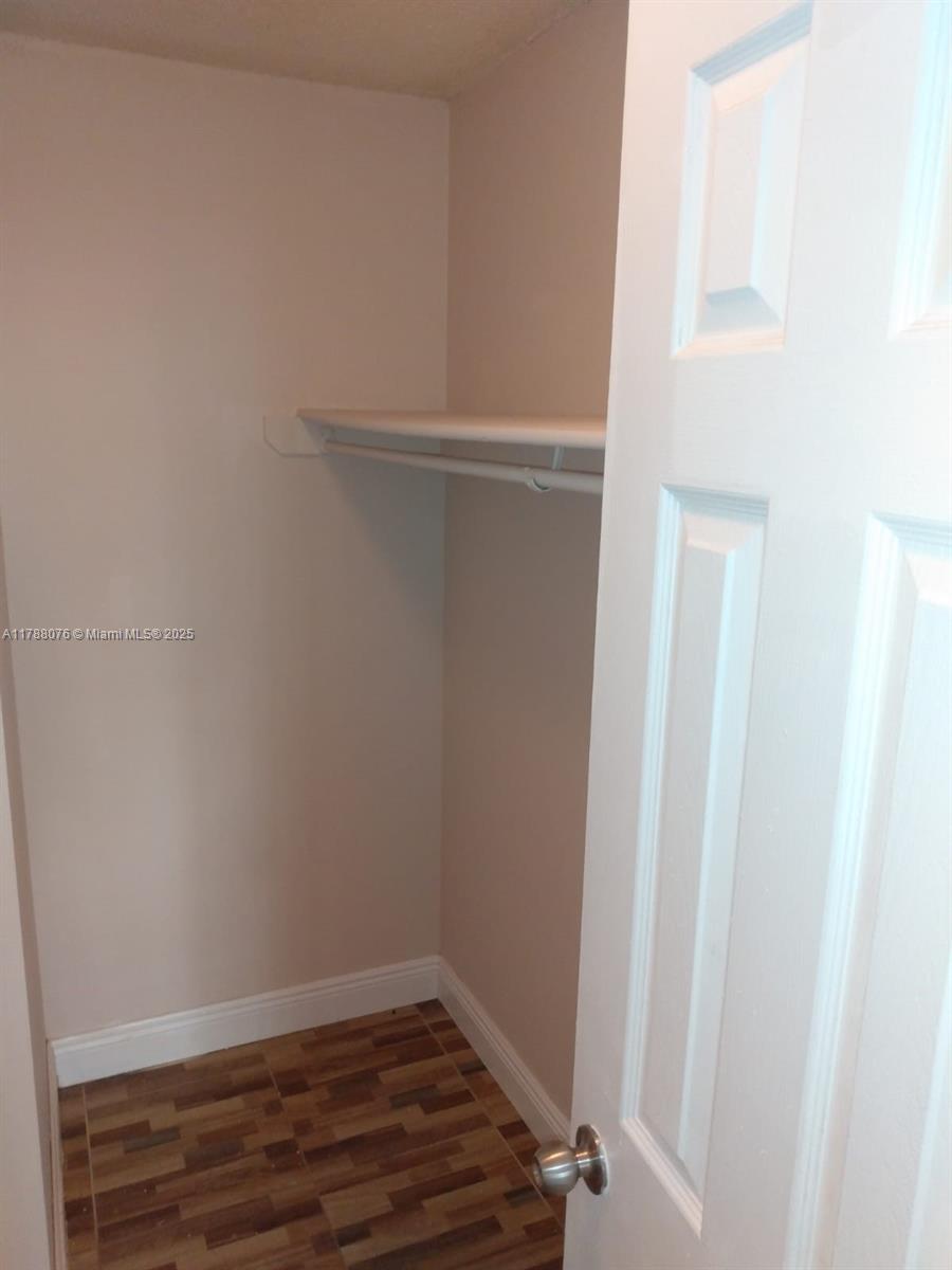A small closet features a white shelf, a hanging rod, and wood-look tile flooring — 494 NW 165th St Rd # 102, Miami FL 33169, MIAMI, FL