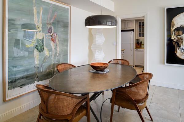 A dining room features an oval table, rattan chairs, and large artwork on white walls — 250 Bradley Place # 609, Palm Beach FL 33480, PALM BEACH, FL