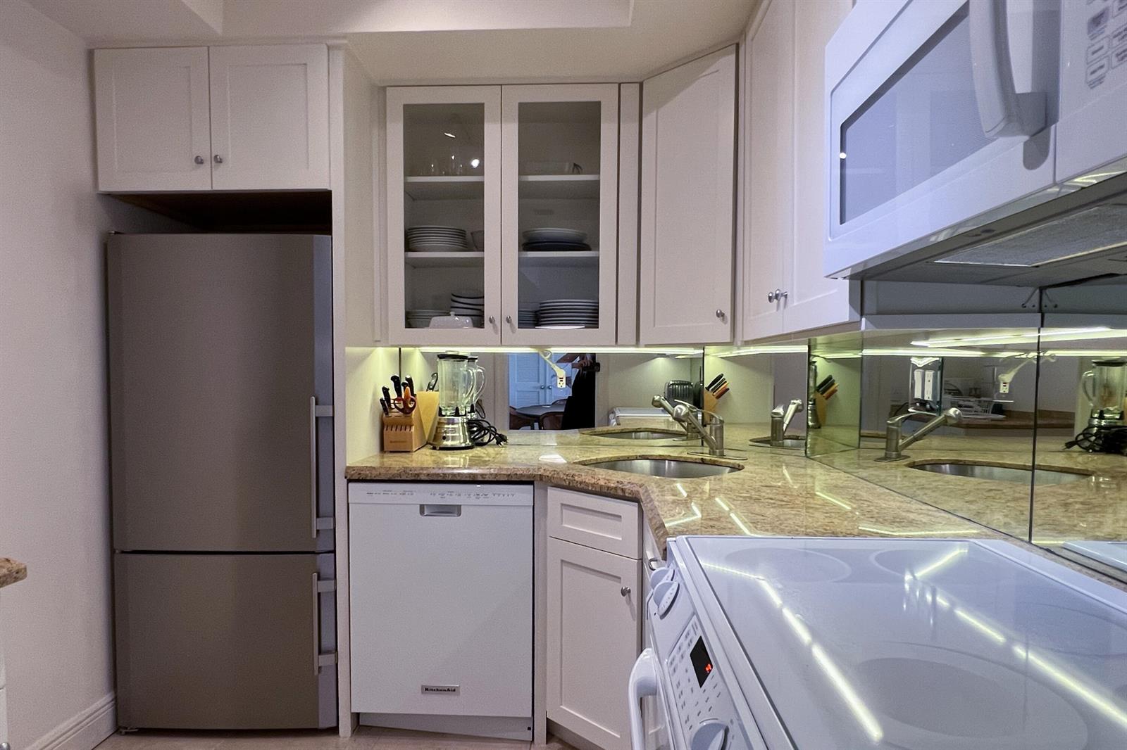 A kitchen features white cabinets, stainless steel appliances, granite countertops, and a mirrored backsplash — 250 Bradley Place # 609, Palm Beach FL 33480, PALM BEACH, FL