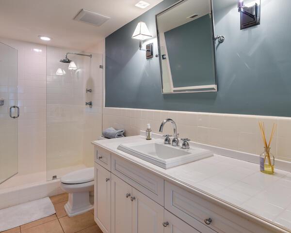 A bathroom features a white vanity, a tiled countertop, a glass shower, and blue walls — 250 Bradley Place # 609, Palm Beach FL 33480, PALM BEACH, FL