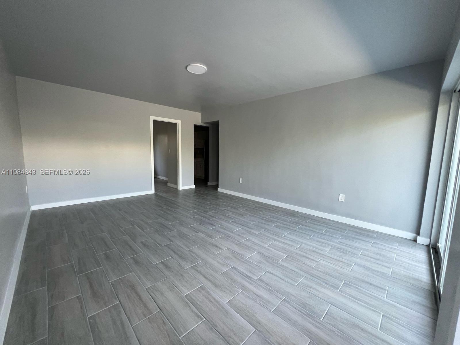 An empty room features gray walls, wood-look tile flooring, and a sliding glass door — 161 NE 117th St, Miami FL 33161, MIAMI, FL