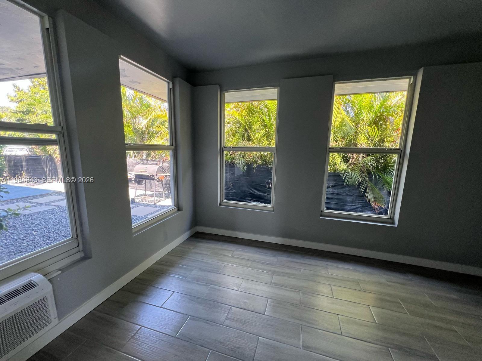A room with gray walls, wood-look tile flooring, and multiple windows overlooking a backyard — 161 NE 117th St, Miami FL 33161, MIAMI, FL