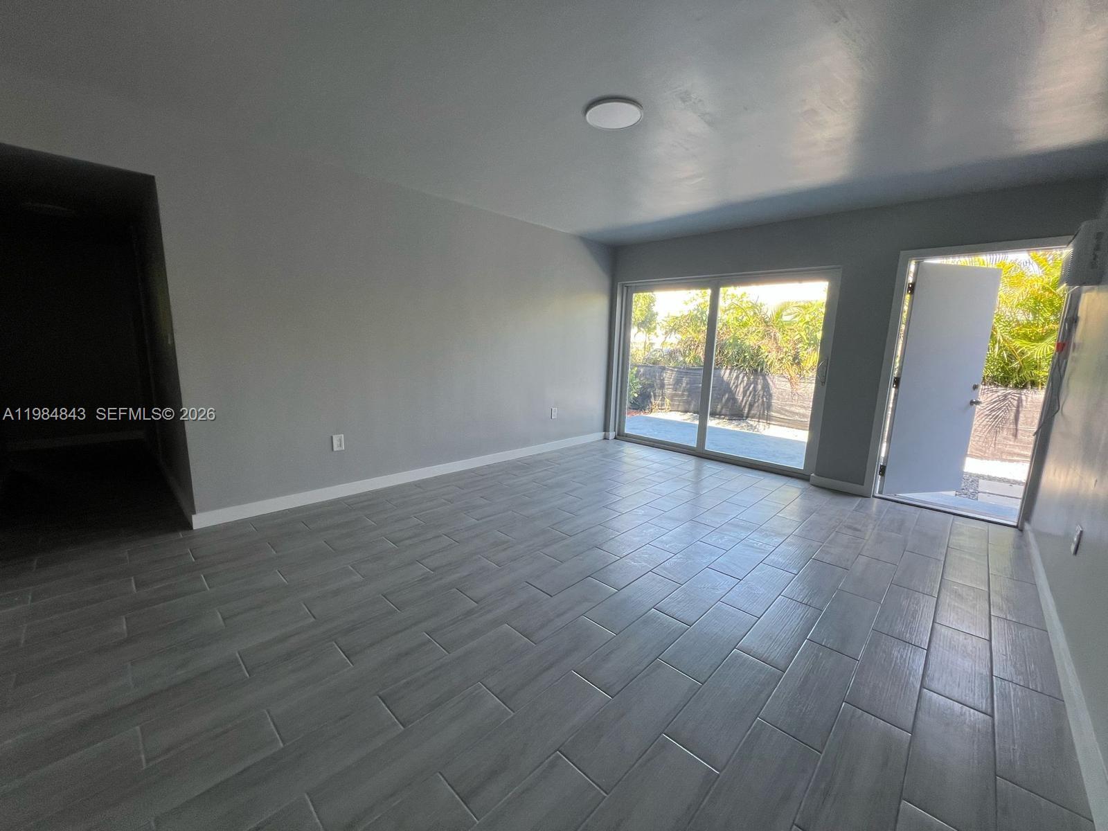 An empty room features gray tile flooring, light gray walls, a sliding glass door, and an exit — 161 NE 117th St, Miami FL 33161, MIAMI, FL