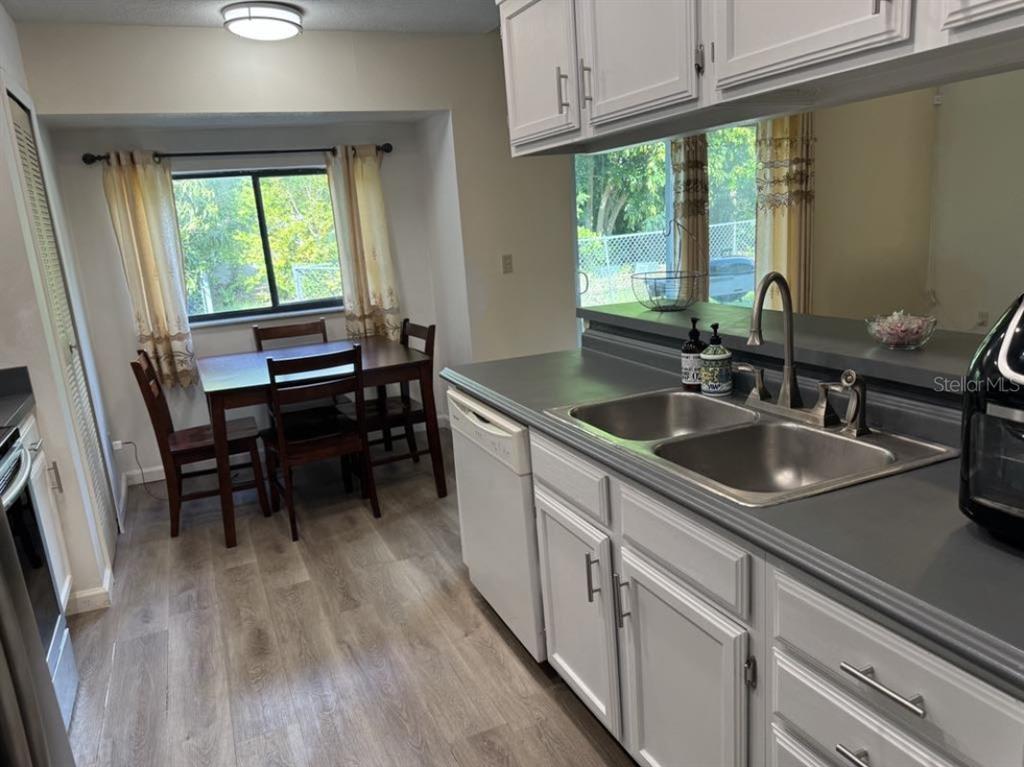 A kitchen with white cabinets, gray countertops, and a stainless steel sink overlooks a dining area — 5523 WESTVIEW DRIVE, ORLANDO, FL