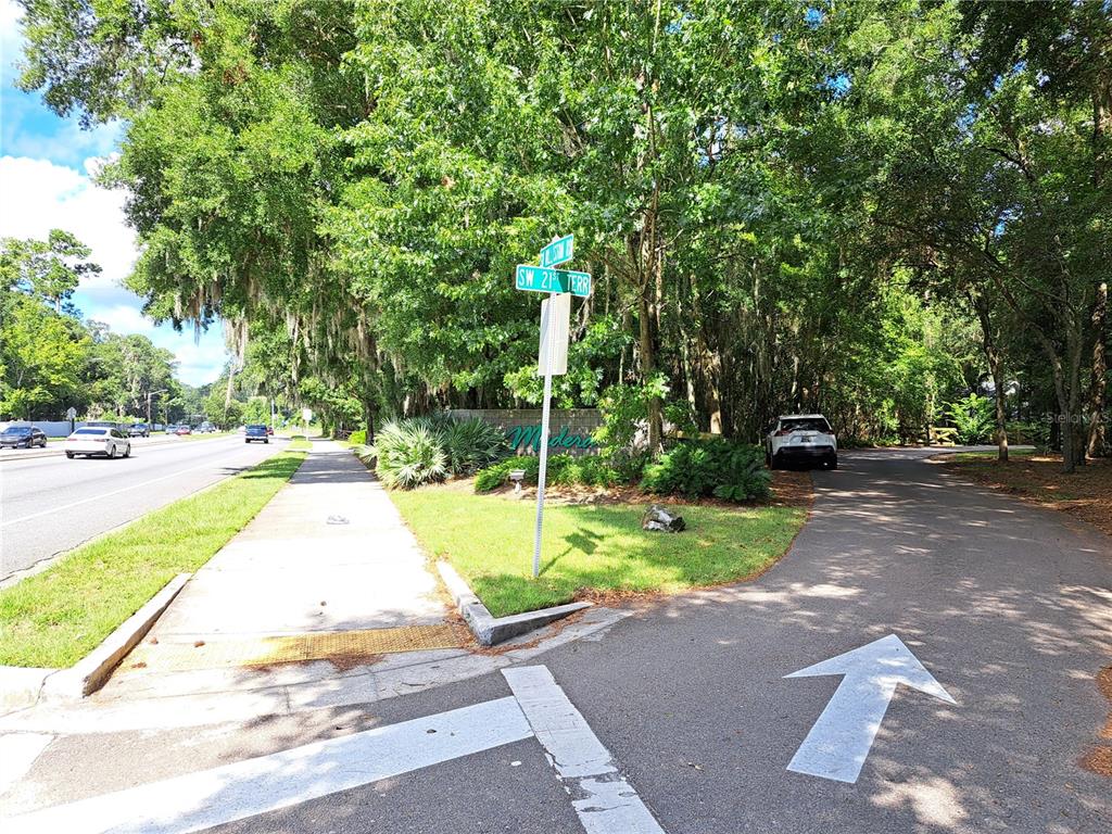 A street corner with a sidewalk, road signs, and a driveway leading into a wooded area — 2164 SW 37TH COURT, GAINESVILLE, FL
