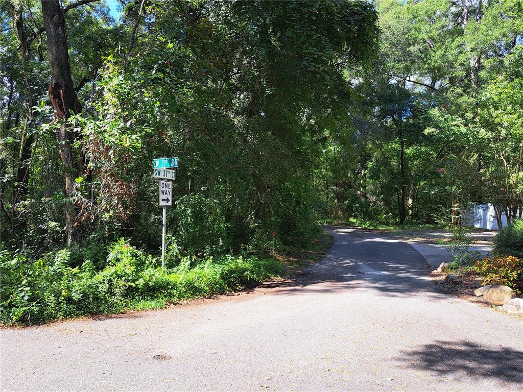 A street sign stands at the corner of a paved road surrounded by dense trees — 2164 SW 37TH COURT, GAINESVILLE, FL