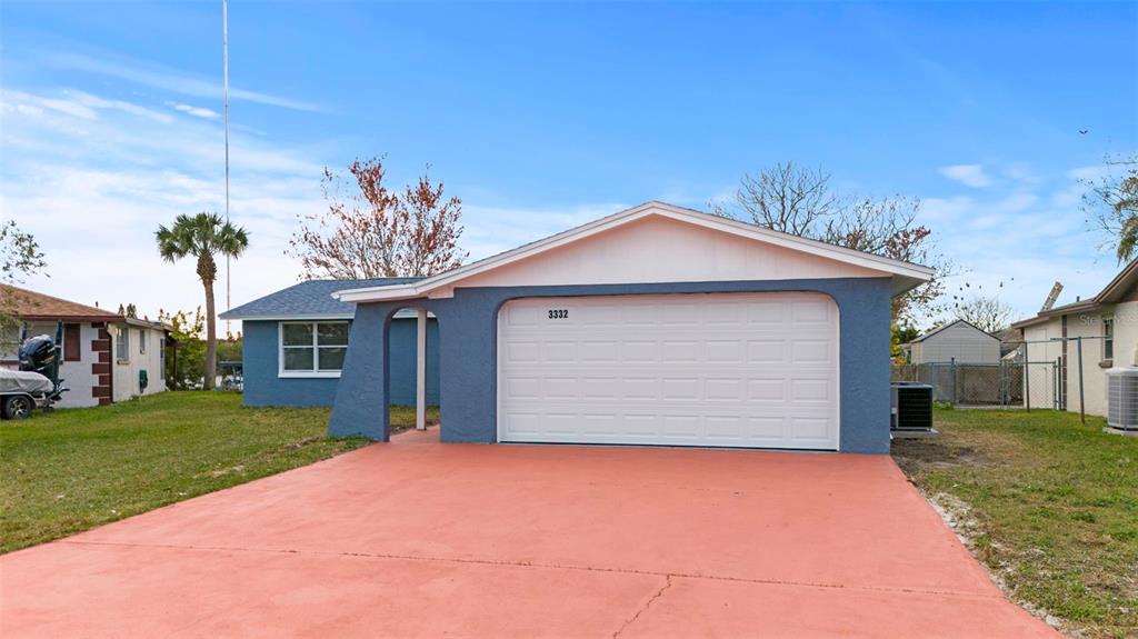 A blue single-story house features a white garage door and a red concrete driveway — 3332 WILSON DRIVE, HOLIDAY, FL