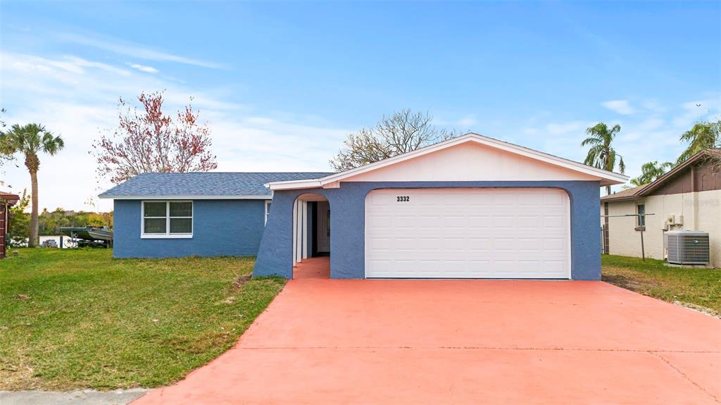 A blue single-story house features a white garage door and a coral-colored concrete driveway — 3332 WILSON DRIVE, HOLIDAY, FL