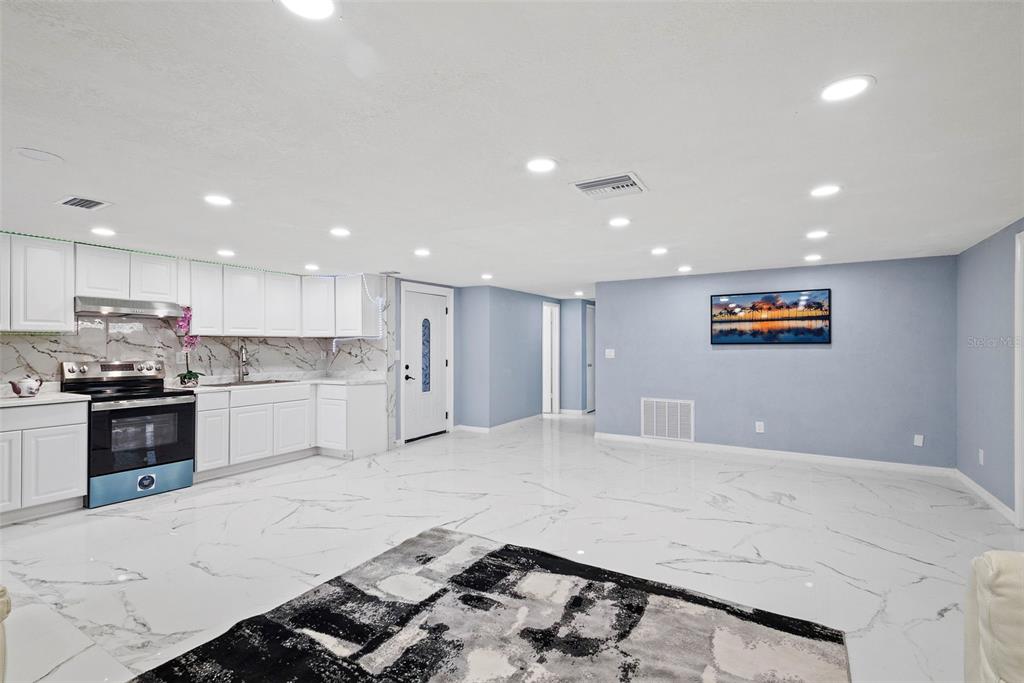A kitchen and living area featuring white cabinets, marble-patterned tile floors, and light blue walls — 3332 WILSON DRIVE, HOLIDAY, FL