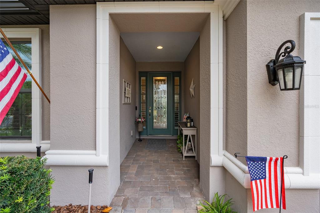 A covered entryway features a teal front door, stone pavers, and two American flags — 1389 ZEEK RIDGE STREET, CLERMONT, FL
