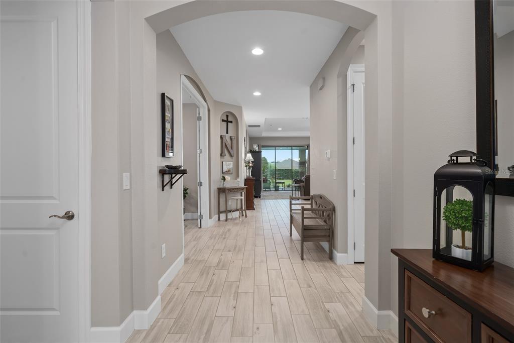 A bright hallway with light wood-look tile flooring leads toward a glass-doored living area — 1389 ZEEK RIDGE STREET, CLERMONT, FL