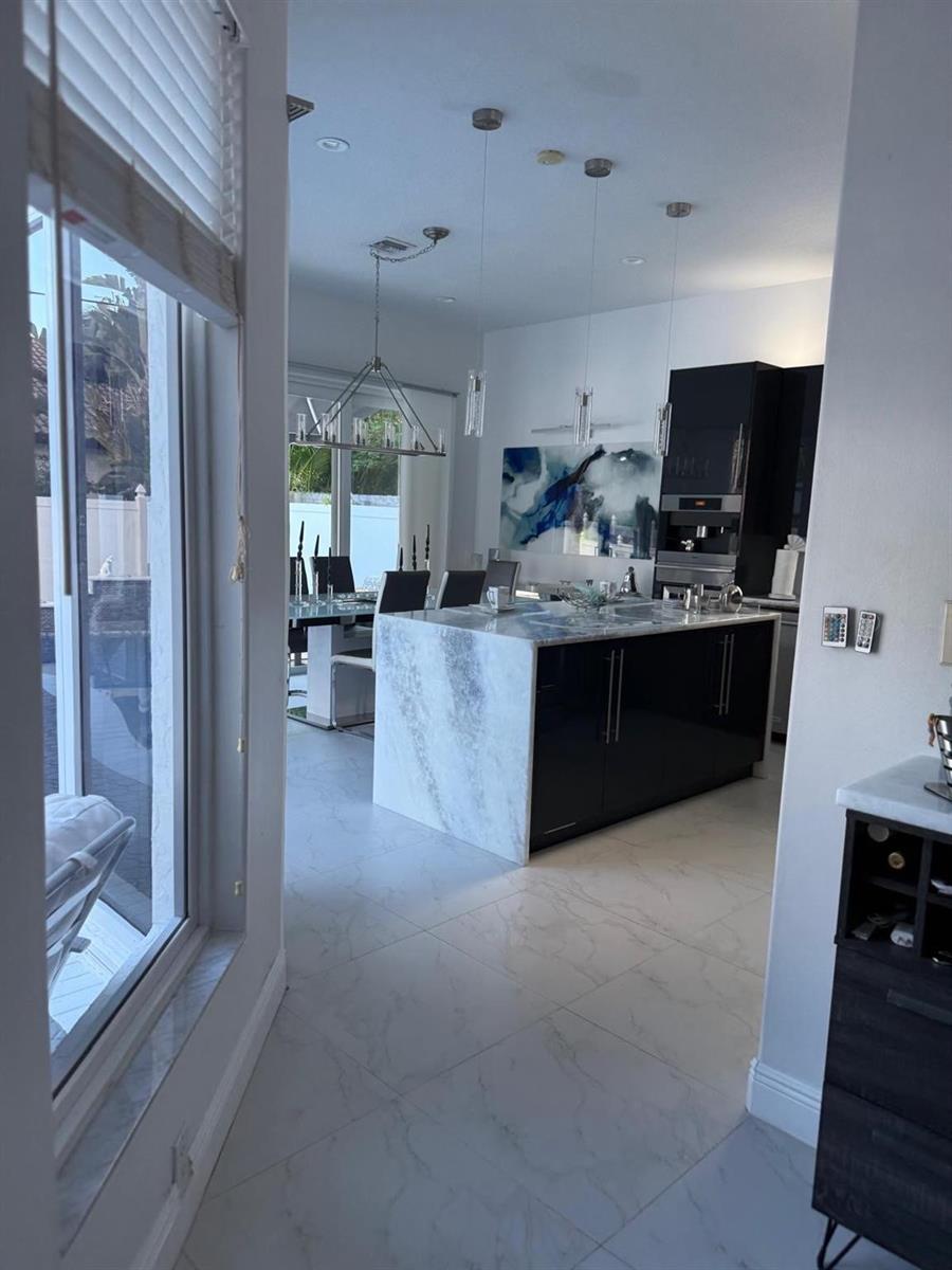 A modern kitchen features a marble waterfall island, black cabinetry, and tile flooring — 830 Bailey Street, Boca Raton FL 33487, BOCA RATON, FL