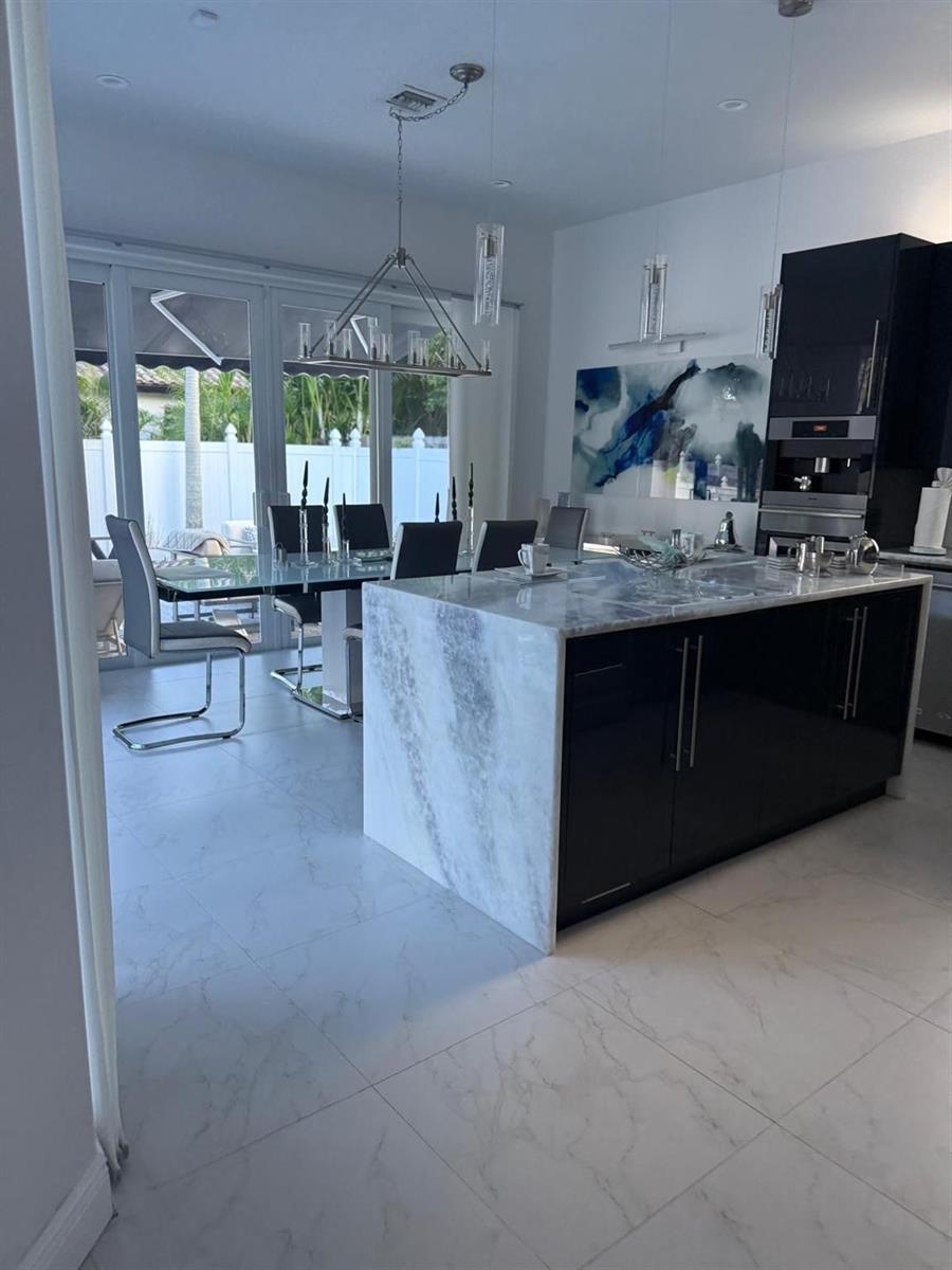 A modern kitchen features a marble waterfall island, black cabinetry, and an adjacent dining area — 830 Bailey Street, Boca Raton FL 33487, BOCA RATON, FL
