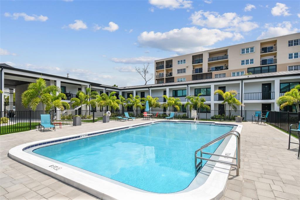 A rectangular swimming pool sits in a paved courtyard surrounded by a multi-story apartment building — 2942 W BAY DRIVE UNIT 36, BELLEAIR BLUFFS, FL