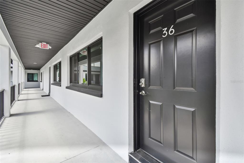A black door numbered 36 opens onto a covered outdoor walkway with white walls — 2942 W BAY DRIVE UNIT 36, BELLEAIR BLUFFS, FL