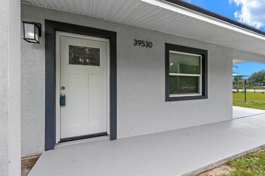A white front door with a glass insert sits next to a window on a porch — 39530 LINCOLN AVENUE, ZEPHYRHILLS, FL
