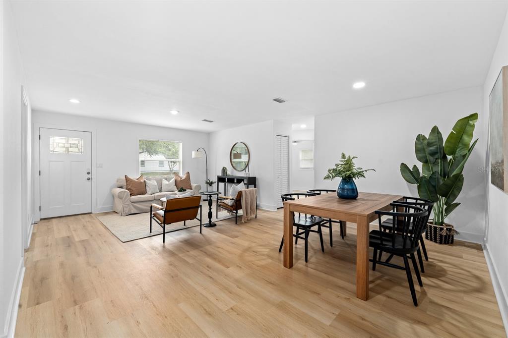 An open-concept living and dining area features light wood flooring, white walls, and modern furniture — 39530 LINCOLN AVENUE, ZEPHYRHILLS, FL