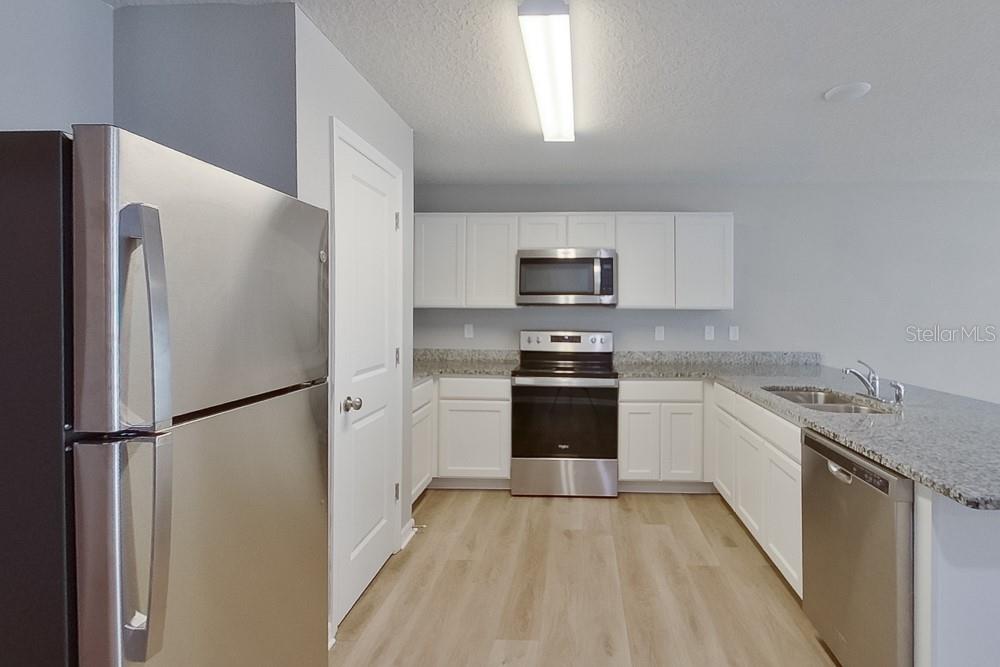 A kitchen features stainless steel appliances, white cabinets, granite countertops, and light wood-look flooring — 1924 W ROSEBORO DRIVE, DUNNELLON, FL